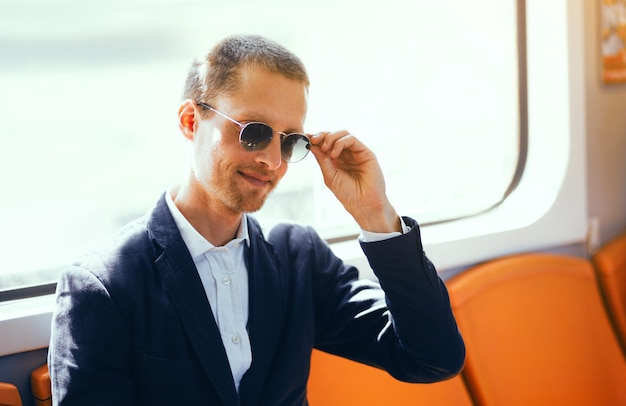 Zakenman in zonnebril op metro Knappe man van middelbare leeftijd met shirt en jas die zijn zonnebril vastmaakt terwijl hij in de metro zit