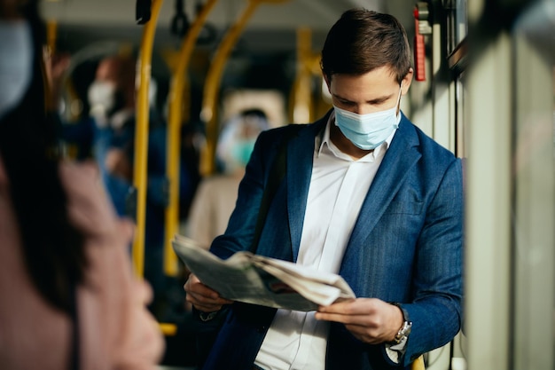 Zakenman met beschermend gezichtsmasker krant lezen tijdens het woon-werkverkeer met de bus
