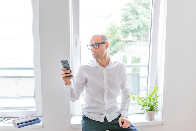 Zakenmanzitting voor bureauvenster die cellphone gebruiken