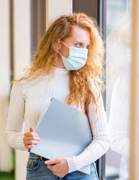 Gratis foto zakenvrouw die een masker draagt en documenten vasthoudt