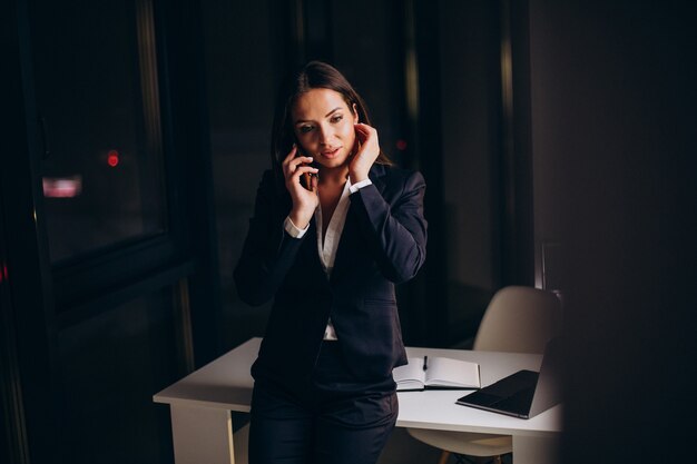 Zakenvrouw die telefoon op kantoor gebruikt en 's avonds laat blijft staying
