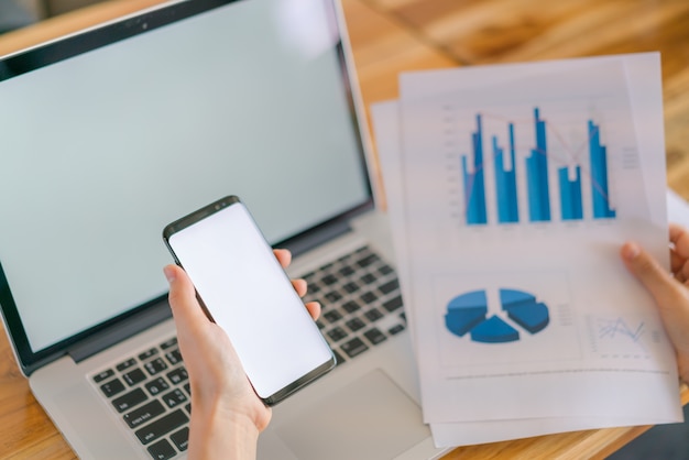 Zakenvrouw hand met Financial charts en mobiele telefoon over laptop op de tafel.