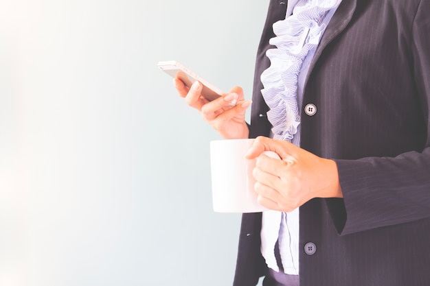 Zakenvrouw in donker pak met mobiele telefoon en kopje koffie, business concept met kopie ruimte