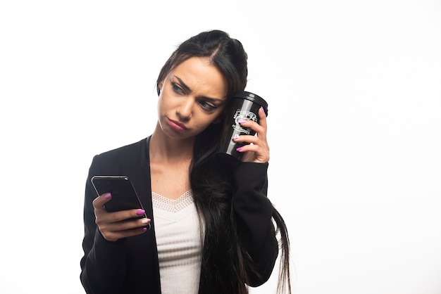 Zakenvrouw met een kopje en een mobiele telefoon op een witte muur