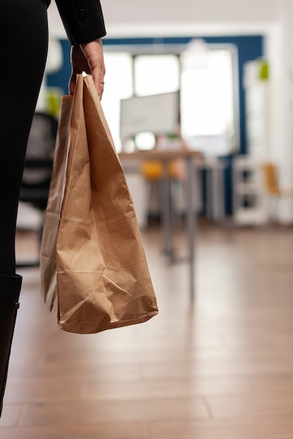 Zakenvrouw met een papieren zak met afhaalmaaltijden die op het bureau wordt gezet tijdens de afhaallunch in het bedrijfskantoor