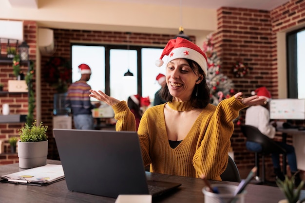 Zakenvrouw praten over videocall conferentie in kantoor met kerstboom en feestelijke decoraties. Bijwonen van teleconferentiegesprekken op afstand en onlinevergaderingen tijdens de vakantieperiode op het werk.