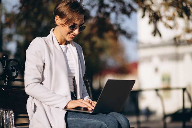 Zakenvrouw zittend op een bankje in het park, werken op de computer