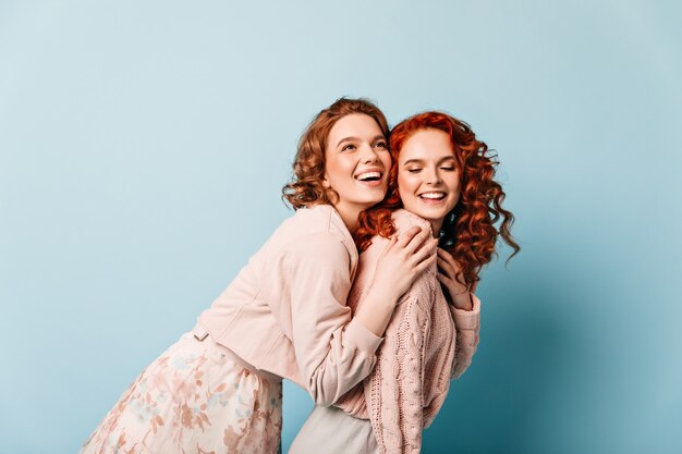 Zalig meisje omarmen gembervriend. Studio shot van twee charmante dames die zich voordeed op blauwe achtergrond.