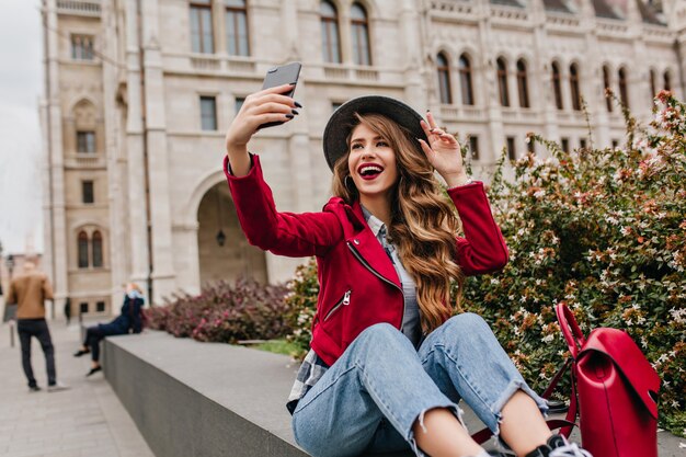 Zalig wit vrouwelijk model in retro jeans die selfie met glimlach maakt