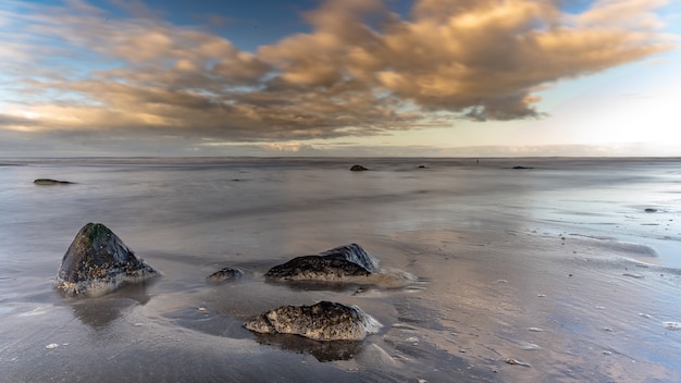 Gratis foto zee met rotsen onder een blauwe bewolkte hemel