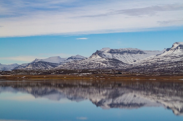 Zee omgeven door rotsachtige bergen bedekt met de sneeuw en nadenken over het water in IJsland