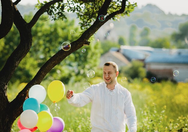 Zeepballonnen vliegen rond een man die onder groene boom staat