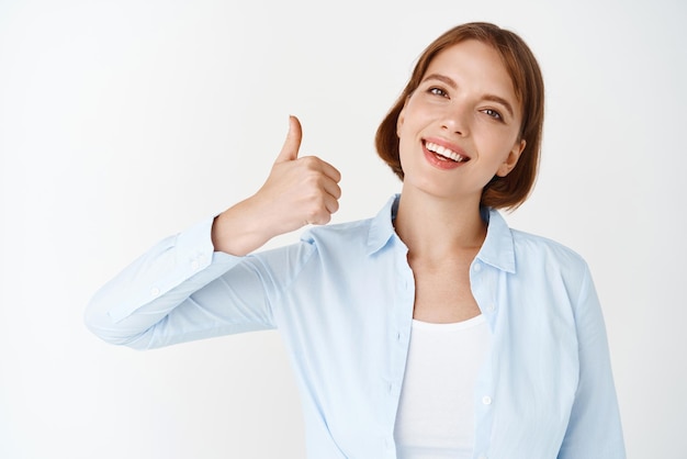 Zeer goed portret van een zakenvrouw die duim omhoog laat zien en goedkeurt, zeg ja en ga ermee akkoord dat je in een blouse op een witte achtergrond staat