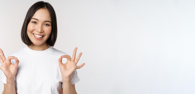 Zeer goed uitstekend Glimlachende aziatische vrouw die oke tekengoedkeuring toont ok gebaar die tevreden kijkt die iets aanbeveelt die over witte achtergrond staat