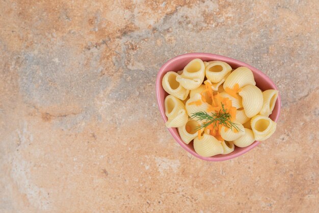 Zeeschelpvormige pasta met plakjes wortel en dille in kom.