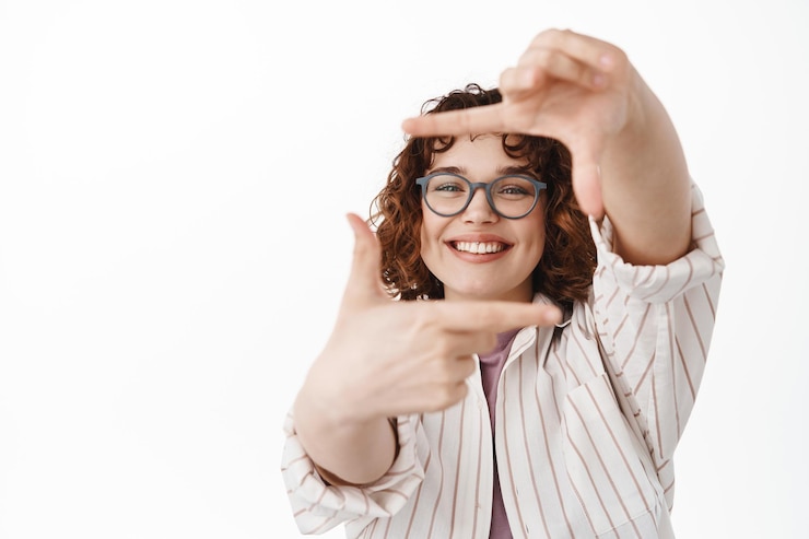 Gratis Foto zeg kaas. gelukkig authentieke jonge vrouw in glazen, kijkend door hand fotolijsten gebaar en lachend met witte tanden brede glimlach, mooie moment, witte achtergrond afbeelden