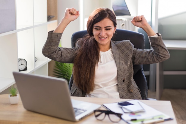 Zegevierende onderneemster bij bureau met laptop