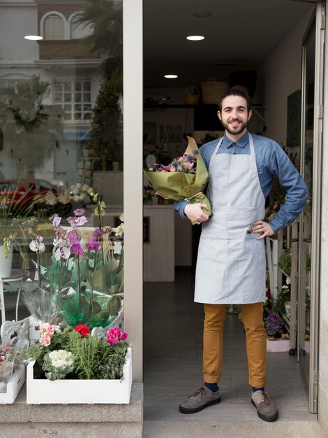 Zekere glimlachende jonge mannelijke bloemist die zich bij de ingang van de holdingsboeket van de bloemwinkel ter beschikking bevinden