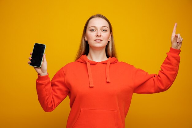 Zekere jonge blonde vrouw die mobiele telefoon houdt die benadrukt