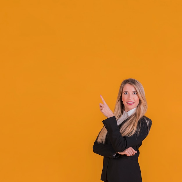 Gratis foto zekere jonge onderneemster die haar vinger omhoog tegen een oranje achtergrond richt