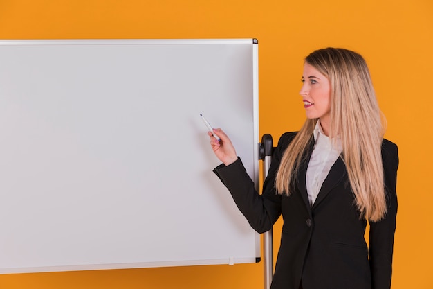 Gratis foto zekere jonge onderneemster die presentatie op whiteboard geeft tegen een oranje achtergrond