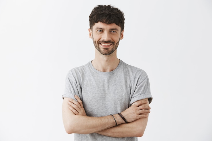 Gratis Foto zekerzinnige knappe man poseert tegen de witte muur.