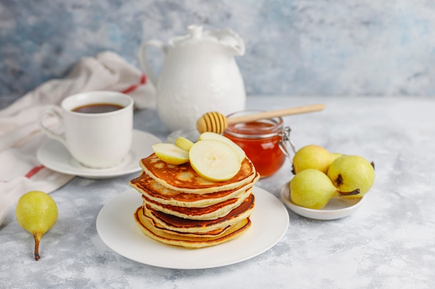 Zelfgemaakt ontbijt: Amerikaanse pannenkoeken geserveerd met peren en honing met een kopje thee op beton. Bovenaanzicht en kopiëren