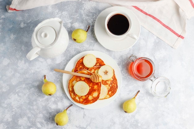 Zelfgemaakt ontbijt: Amerikaanse pannenkoeken geserveerd met peren en honing met een kopje thee op beton. Bovenaanzicht en kopiëren