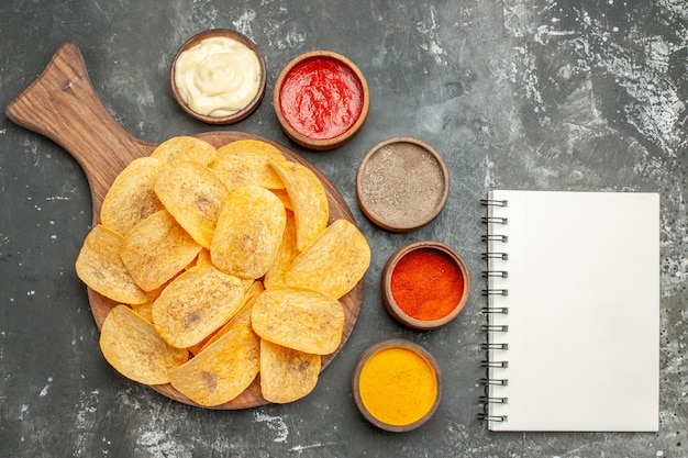 Zelfgemaakte chips kruiden en mayonaise met ketchup op snijplank en notebook op grijze tafel