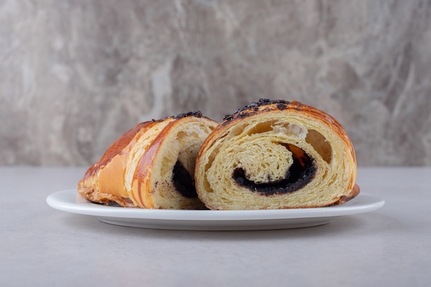 Zelfgemaakte gesneden croissant met chocolade op een bord op marmeren tafel.