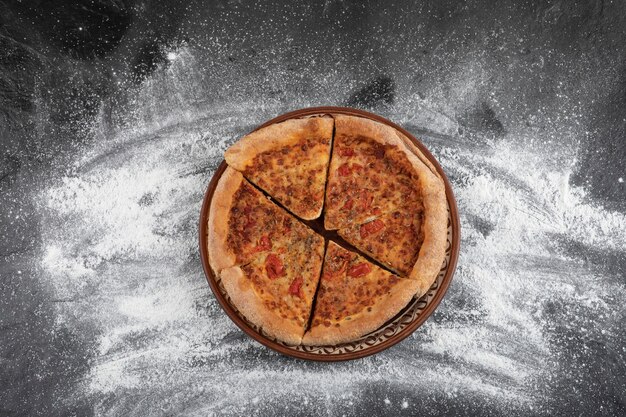 Zelfgemaakte gesneden pizza op bruine plaat op zwarte ondergrond