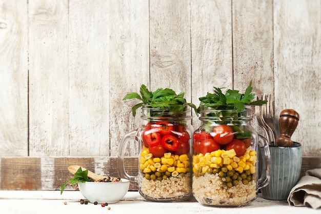 Zelfgemaakte gezonde layer salade in mason potjes op een houten backgroun