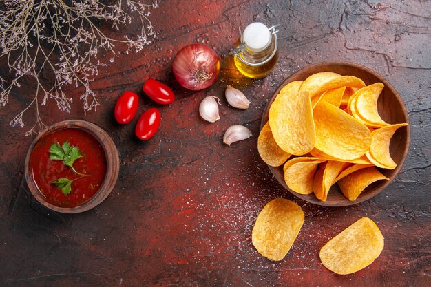 Zelfgemaakte heerlijke knapperige aardappelchips binnen en buiten de bruine potoliefles ketchup tomaten knoflookui op donkere achtergrond