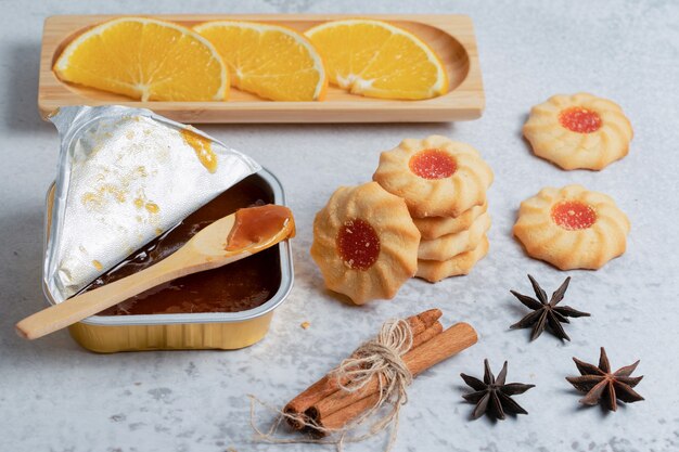 Zelfgemaakte jam en koekjes met stukjes sinaasappel en kaneel over grijze ondergrond.