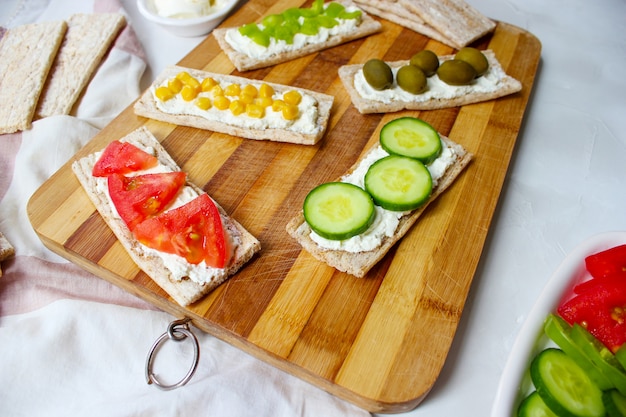 Zelfgemaakte knäckebröd toast met kwark en groene olijven, plakjes kool, tomaten, maïs, groene peper op snijplank. Gezond voedselconcept, Hoogste mening. Plat leggen