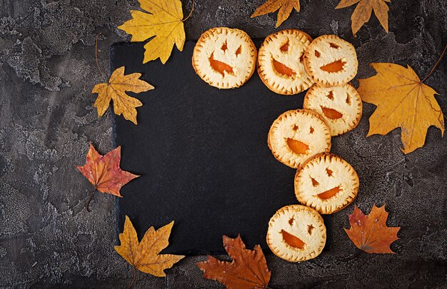 Zelfgemaakte koekjes in de vorm als Halloween-hefboom-o-lantaarnpompoenen op de donkere lijst. Bovenaanzicht