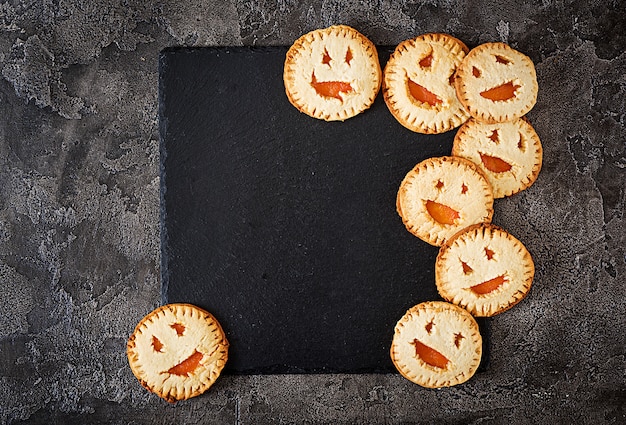 Zelfgemaakte koekjes in de vorm als Halloween-hefboom-o-lantaarnpompoenen op de donkere lijst. Bovenaanzicht