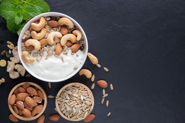 Zelfgemaakte muesli of muesli, kom haver muesli met yoghurt, amandel, cashewnoten, munt en noten op het zwarte rotsbord voor gezond ontbijt, kopieer ruimte. Gezond ontbijtmenuconcept.