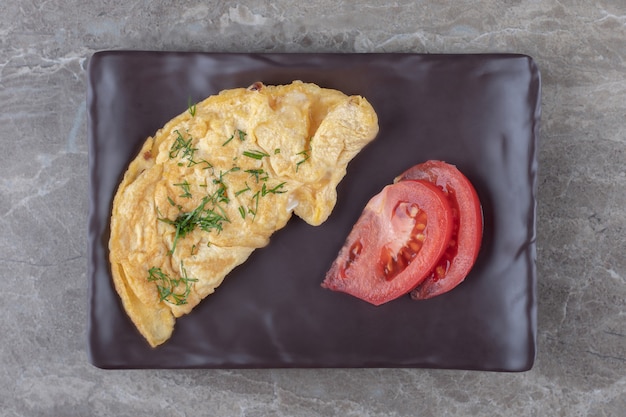 Zelfgemaakte smakelijke omelet met tomaat op donkere plaat.
