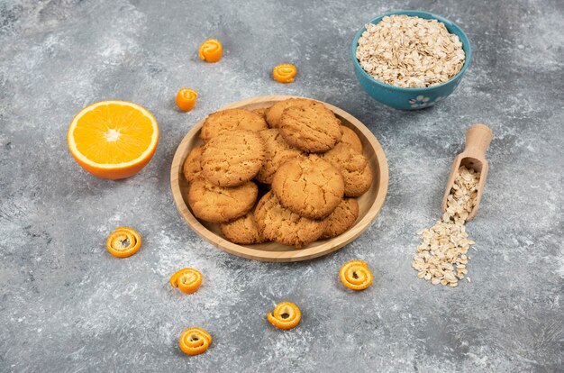 Zelfgemaakte verse koekjes op een houten bord en havermout met sinaasappelen over grijze ondergrond.