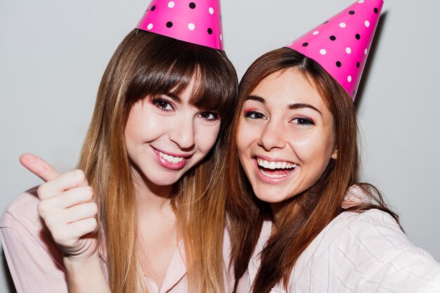 Zelfportret van twee vrouwen in roze papieren verjaardagshoedjes. Vrienden die roze pyjama's dragen