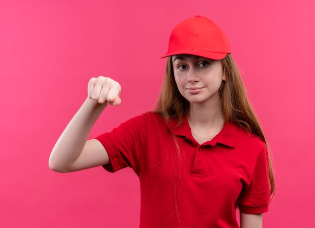 Zelfverzekerd jong bezorgmeisje in rood uniform doet klopgebaar op geïsoleerde roze ruimte