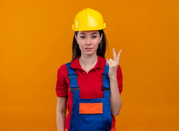 Zelfverzekerd jong bouwersmeisje toont twee vingergebaar op geïsoleerde oranje achtergrond met exemplaarruimte