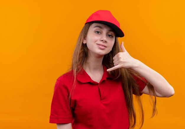 Zelfverzekerd jong leveringsmeisje in rood uniform die vraaggebaar op geïsoleerde oranje ruimte met exemplaarruimte doet