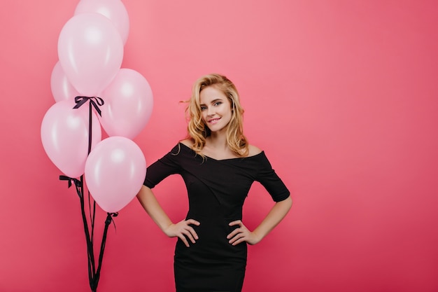 Zelfverzekerd meisje in een mooie jurk genieten van evenement. geïnteresseerde blonde dame met roze ballonnen die geluk uitdrukken.