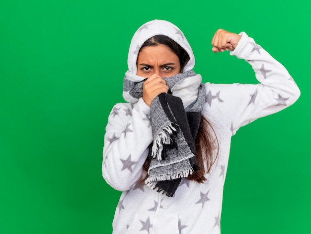 Zelfverzekerd ziek meisje kap wearin sjaal en bedekt gezicht met sjaal zetten en sterke gebaar geïsoleerd op groene achtergrond tonen