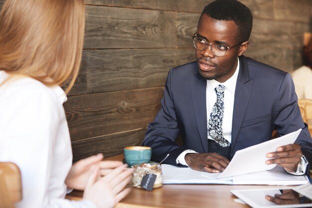 Zelfverzekerde Afrikaanse man in formele slijtage met cv, aandachtig luisterend naar roodharige vrouw