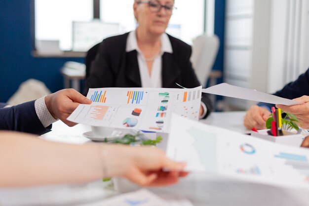 Zelfverzekerde bedrijfsmanager die werktaken geeft aan diverse teamleden die papierwerk analyseren met grafieken in het opstartkantoor