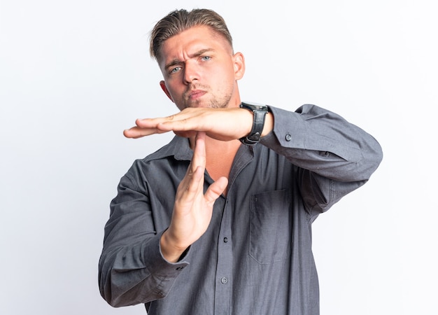 Zelfverzekerde blonde knappe man gebaren time-out teken geïsoleerd op een witte muur met kopie ruimte