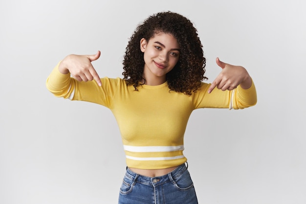 Zelfverzekerde coole brutaal gekrulde brunette vrouwelijke student stijlvolle bijgesneden trui kantelend hoofd glimlachend zelfverzekerd naar beneden wijzende wijsvingers verzekerd dat je van promo-exemplaarruimtepresentatie houdt